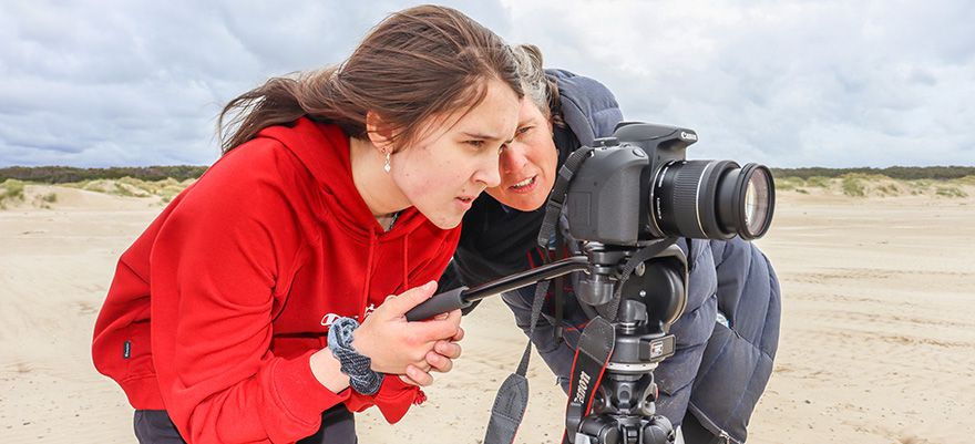 Student on a beach at Circular Head standing behind a camera and tripod learning photography with a mentor