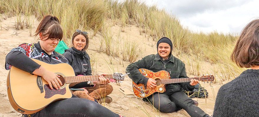 students and musicians learning to play guitar at the beach