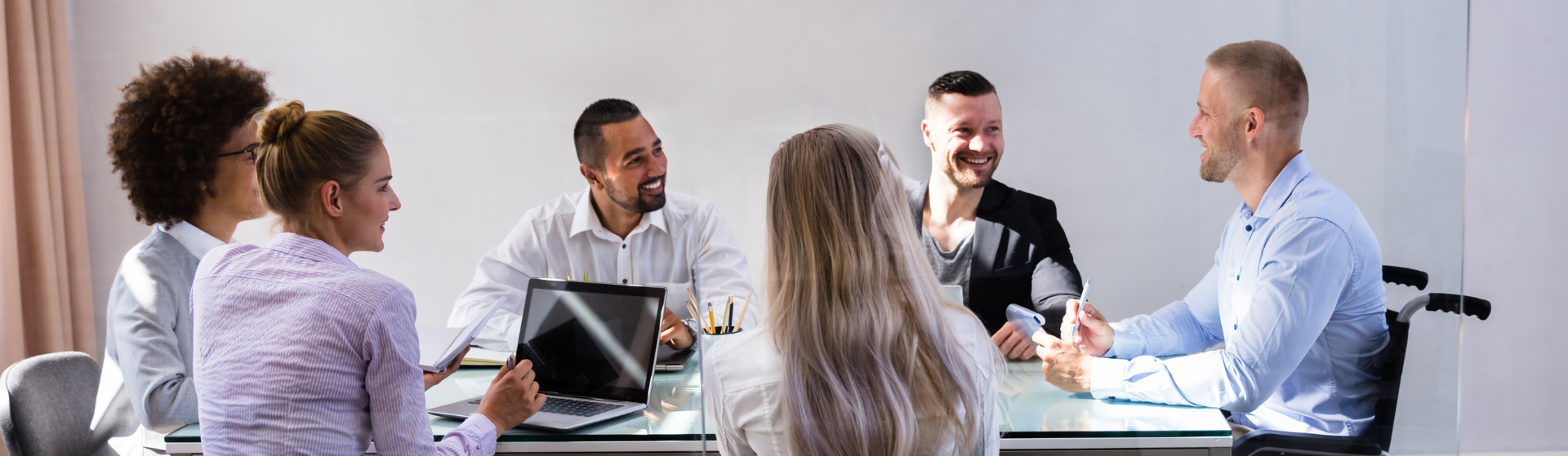 A group of people sitting at an office desk. The person on the end is sitting in a wheelchair