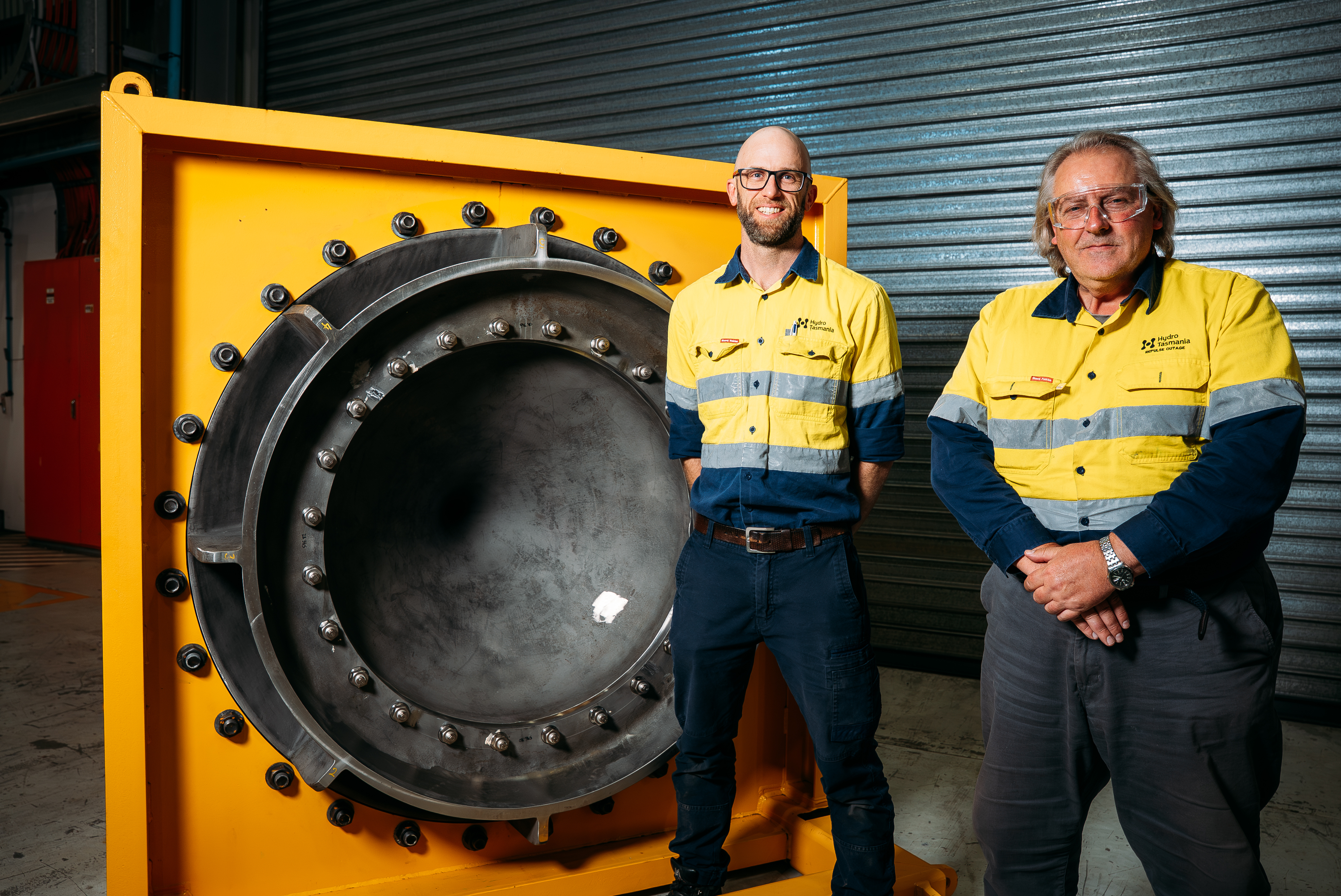 Two men in hi-vis vests stand next to a turbine relief valve