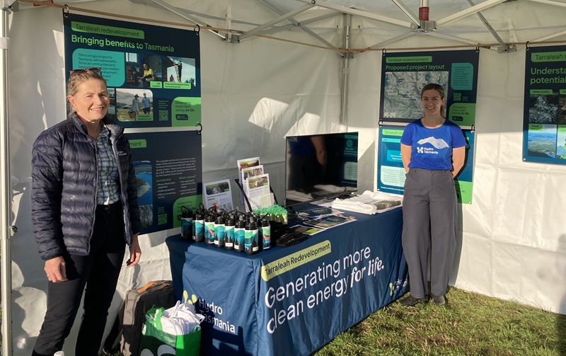 Two people standing in a marquee in front of a table filled with booklets