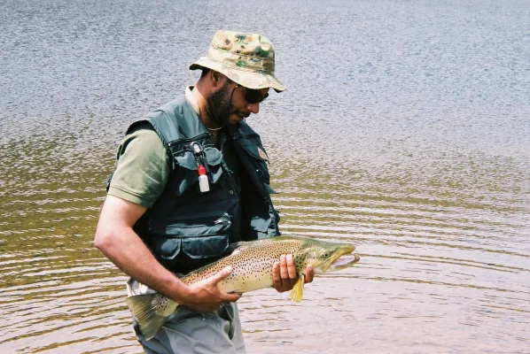 A man in waders standing in the water holding a trout