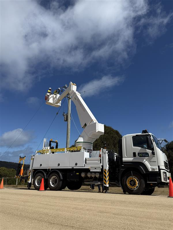 An electrical linesworker installs a powerline while standing at the top of a crane